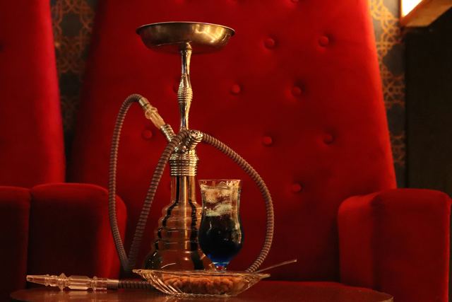 A hookah and a drink on a table beside a red velvet armchair